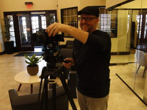 Professional videographer setting up a camera for video ad production in a modern office to create high quality marketing video content.